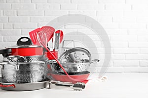 Set of clean kitchenware on white table against brick wall. Space for text