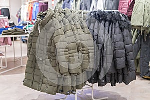 Set of clothes, coat on the rack clothing shop interior on background. Winter jackets in a store