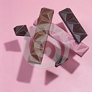 Set of colored chocolate on a pink background. Flying chocolate casts shadows