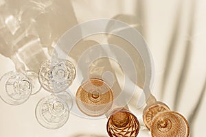 Set colored glasses from transparent and beige glass with beautiful shadows from palm leaf at sunlight, summer drink for