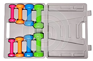 A set of colored isolated dumbbells for sports on a white background is stacked in a gray case from above