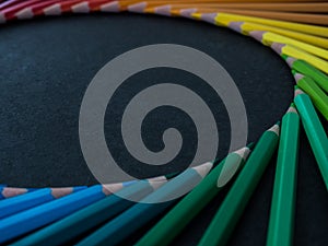 Set of colored pencils arranged in a wheel on slate background