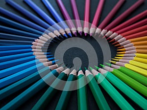 Set of colored pencils arranged in a wheel on slate background