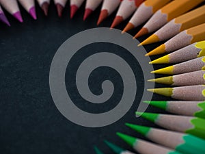 Set of colored pencils arranged in a wheel on slate background