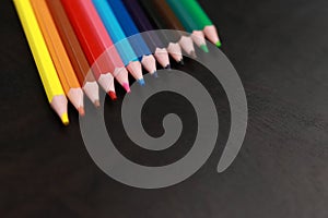 A set of colored pencils on a black wooden background. Sharpened bright pencils
