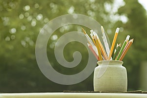 Set of colored pencils in ceramic glass on wooden table with green bokeh background. Back to school concept. Student