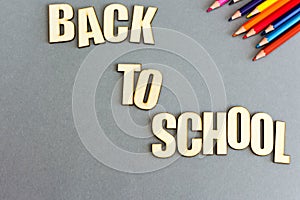 A set of colored pencils on gray background from above. Inscription from wooden letters: back to school. Flat lay, copy