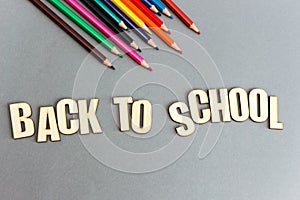 A set of colored pencils on gray background from above. Inscription from wooden letters: back to school. Flat lay, copy