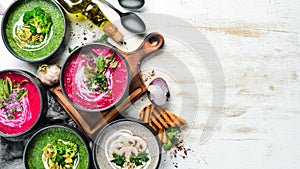 Set of colored soups on white wooden background. Beet soup, broccoli cream soup and mushroom soup.