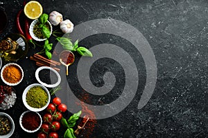 Set of colored spices in bowls and herbs on a black stone background. View from above.