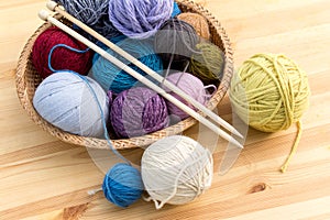 Set of colored yarn balls and needles on straw plate