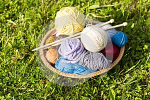 Set of colored yarn balls and needles on straw plate