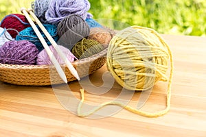 Set of colored yarn balls and needles on straw plate close up