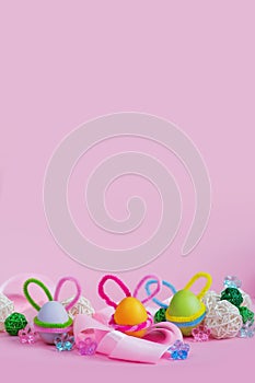 Set of colorful eggs with Easter bunny ears lie near the ribbon and ornaments on a pink background. Vertical banner. Postcard for