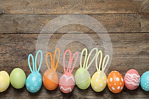 Set of colorful eggs with Easter bunny ears on wooden background, top view.