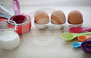 Set of colorful measuring cups, measuring spoons, three eggs and milk in glasses jar.