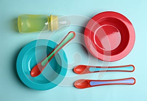 Set of colorful plastic dishware on blue background, flat lay. Serving baby food