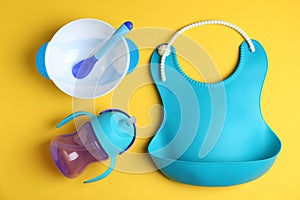 Set of colorful plastic dishware and silicone bib on background, flat lay. Serving baby food