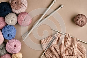 Set of colorful wool yarn and knitting on knitting needles on beige background. Top view