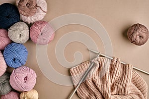 Set of colorful wool yarn and knitting on knitting needles on beige background. Top view