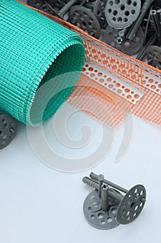 A set of construction items for the insulation of walls. Plastic dowels, a roll of mesh for the insulation of facades and a corne