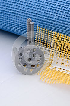 A set of construction items for the insulation of walls. Plastic dowels, a roll of mesh for the insulation of facades and a corner