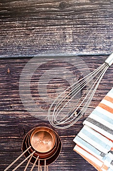 Set of copper measuring cups and whisk with stripe napkin on dark old wood  background