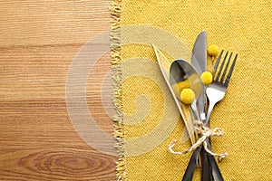 Set of cutlery, yellow cloth and autumnal decor on wooden background, flat lay with space for text. Table setting elements