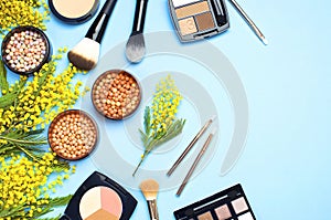 Set of decorative cosmetics for make-up Powder Rouge Eyeshadow Corrector Brushes and flowers of mimosa on blue background. Makeup