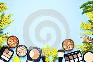 Set of decorative cosmetics for make-up Powder Rouge Eyeshadow Corrector Brushes and flowers of mimosa on blue background. Makeup