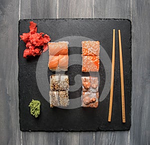 Set of delicious sushi with ginger, soy sauce and wasabi on a black stone tray, on a gray background, top view