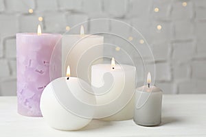 Set of different candles burning on white table