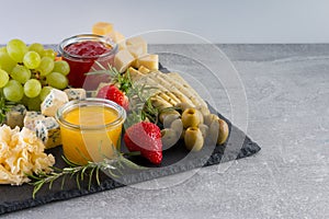 Set of different cheese appetizer with grapes, strawberry, honey and jam on gray background.