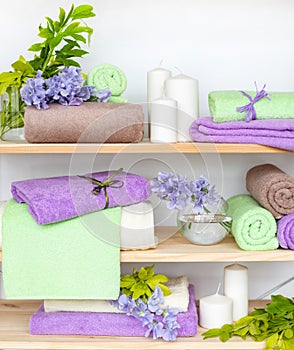 Set of different colors terry towels with blue flowers and candles on wooden shelfs