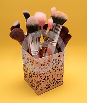 Set of different cosmetic brushes in a pink makeup carrier case on bright yellow background photo