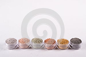 Set of different cosmetic clay mud powders on white