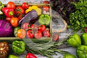 Set of different fresh raw colored vegetables in the wooden tray, light wooden background