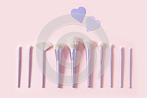 Set of different make up brushes, favourite make up tools on pink background with hearts. Professional make up brushes for