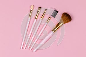 Set of different makeup brushes close-up against a pink pastel background, top view