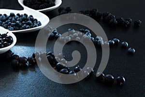 Set of different types of black berries in a white plate on a black table. Stylish seasonal vitamins