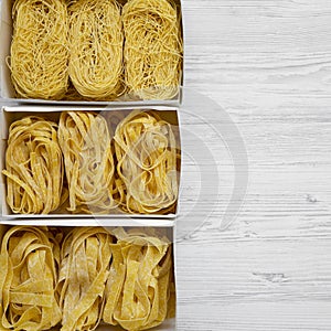Set of different uncooked pasta in paper boxes over white wooden background. Top view. From above, overhead. Copy space