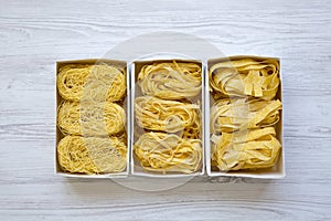 Set of different uncooked pasta in paper boxes on a white wooden table, top view. From above, overhead.