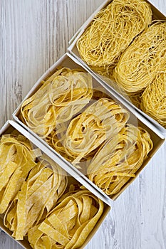 Set of different uncooked pasta in paper boxes on a white wooden table, top view. From above, overhead, flat lay.