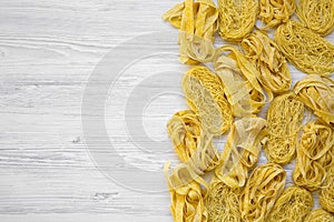 Set of different uncooked pasta on white wooden background, view from above.