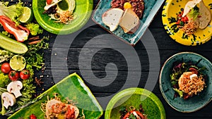 A set of dishes of meat and fresh vegetables and fish on a wooden table.