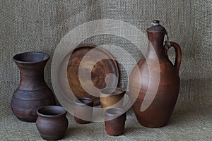 Set of earthenware crockery: jug for wine, round dish, glasses, vase, pot, mug on homemade jute plain cloth. Concept â€” kitchen