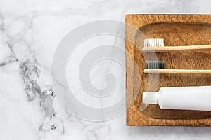 Set of eco-friendly toothbrushes and toothpaste on wooden stand and marble background.