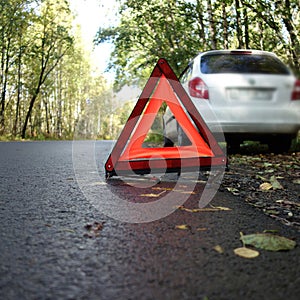 Set emergency stop sign on the road in autumn forest, background white car. concept of roadside and travel assistance