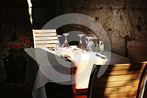 Set empty tables in cozy cafe with empty wine glasses in old european street in summer time without visitors