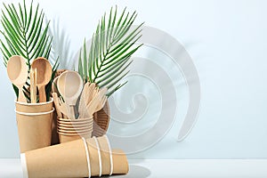 A set of environmentally friendly dishes on a sunny table. Paper cups, plates, kraft paper napkins, barbecue straws, wooden forks